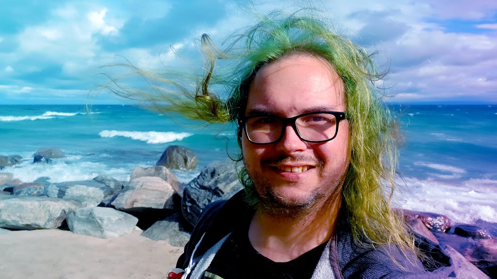 A man with long green hair wearing a hooded sweater vest stands at a breakwater, hair blowing in the wind, Photo 1